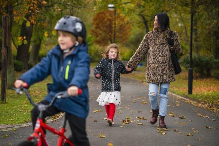 image of cghild cycling in park with mother and sister walking in the background