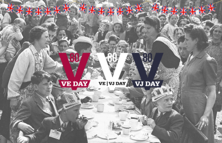 VE Day street party from 1945 with children sat at the table and adults, mainly women, all around enjoying the celebrations