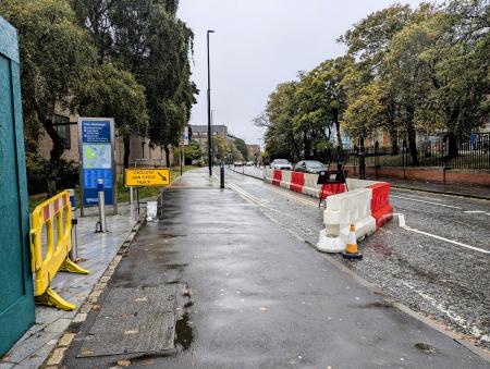 View southbound along Queen Victoria Road with a cycle track on the left of the road, marked by barriers at the end of the track.