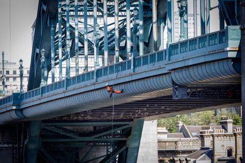 Photo shows the Tyne Bridge with an engineer abseiling down below the deck to carry out vital inspection work.