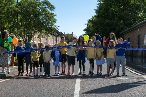 Photo shows children at Hotspur Primary School on a traffic-free street cutting a ribbon to launch their School Streets scheme.