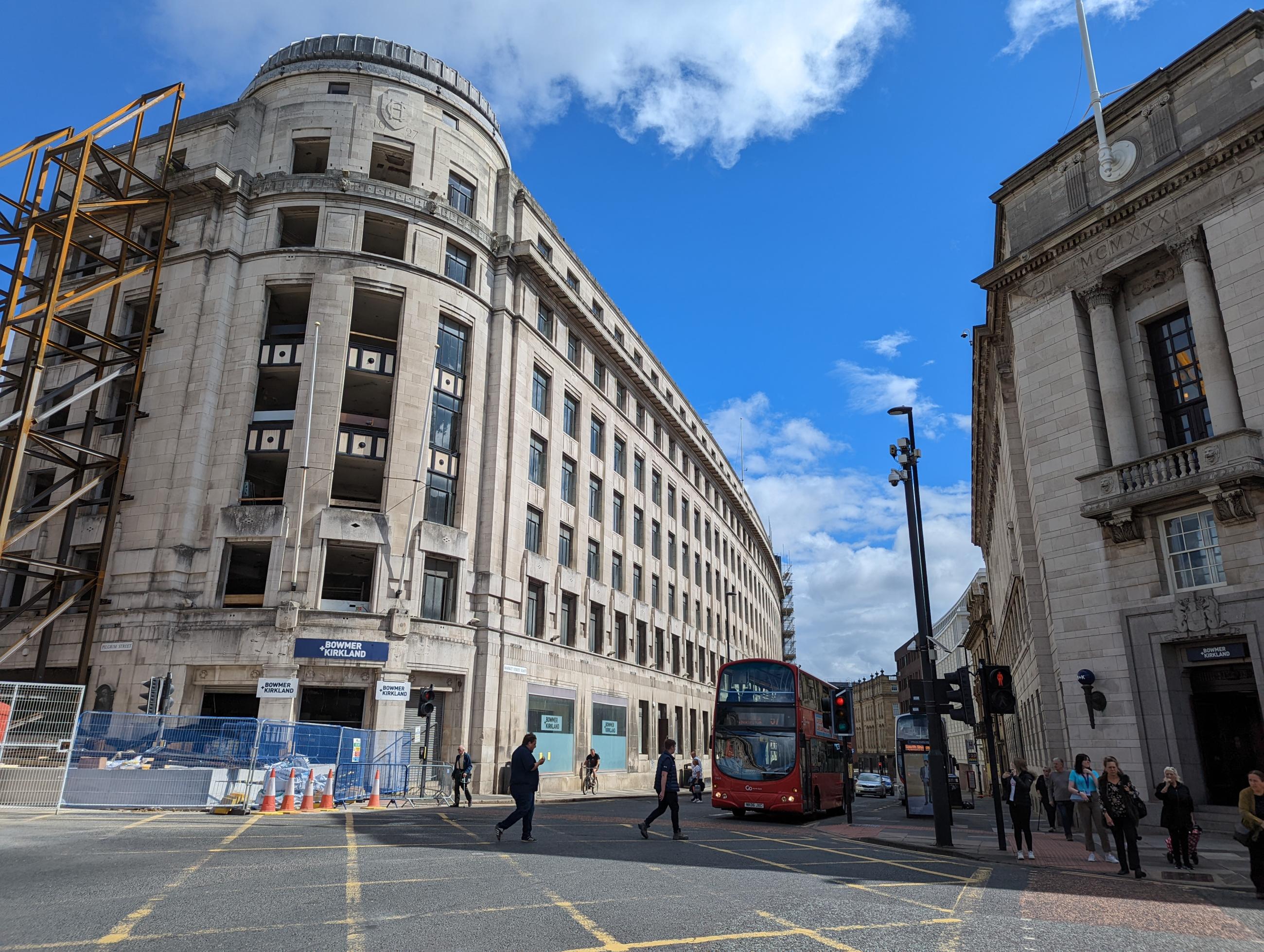 Photo shows the corner of a road junction with tall buildings either side and blue sky.