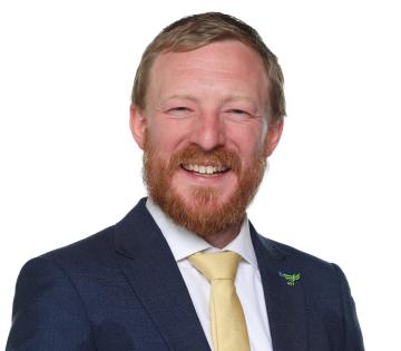 Councillor Colin Ferguson has reddish brown hair, a beard and a moustache. He is wearing a navy jacket, white shirt and pale yellow tie.
