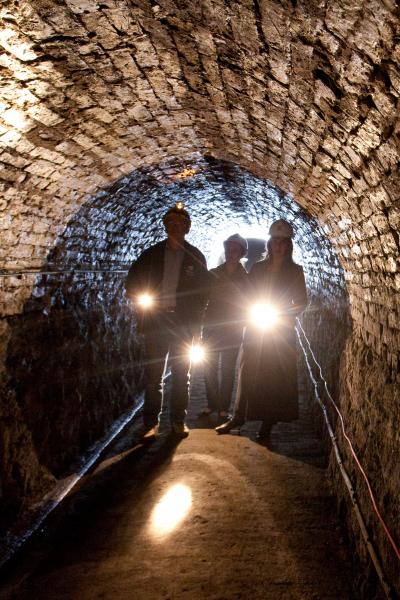 Three people in a tunnel wearing safety hats and carrying electric torches. 